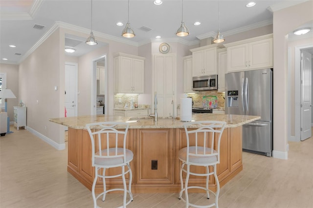 kitchen featuring a kitchen bar, appliances with stainless steel finishes, a kitchen island with sink, and hanging light fixtures