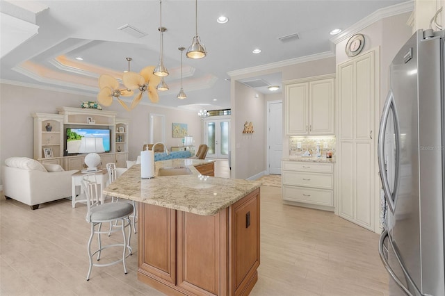 kitchen featuring sink, a large island with sink, light stone countertops, pendant lighting, and stainless steel fridge