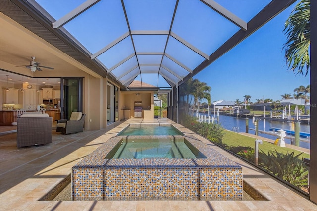 view of swimming pool with an in ground hot tub, a water view, ceiling fan, glass enclosure, and a patio area