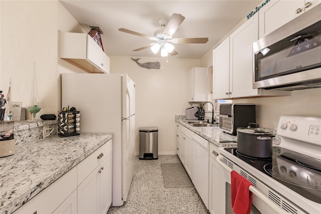 kitchen with white appliances, white cabinetry, ceiling fan, sink, and light stone counters