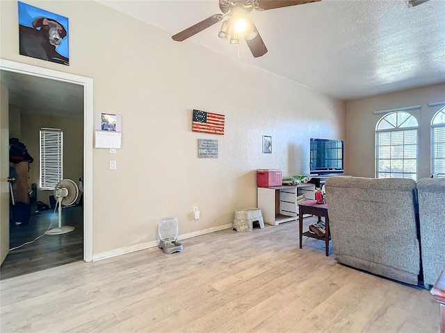 living room featuring ceiling fan, light hardwood / wood-style flooring, and a textured ceiling