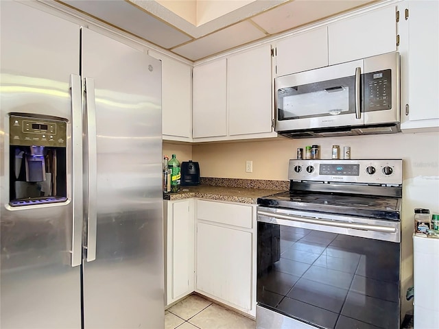 kitchen with stainless steel appliances, light tile patterned flooring, and white cabinets