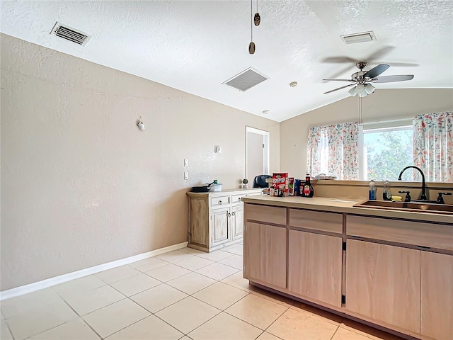 kitchen with light brown cabinetry, sink, vaulted ceiling, a textured ceiling, and light tile patterned floors