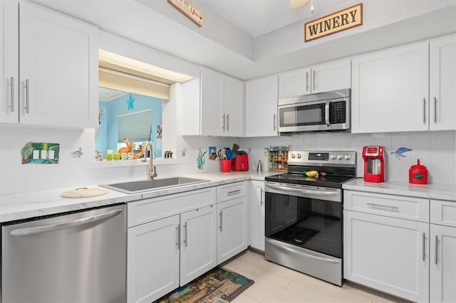 kitchen featuring decorative backsplash, sink, light stone countertops, stainless steel appliances, and white cabinets