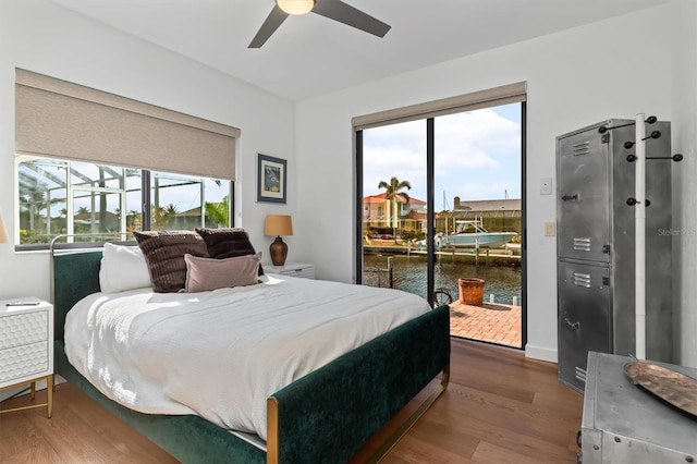 bedroom featuring ceiling fan, a water view, hardwood / wood-style flooring, and multiple windows