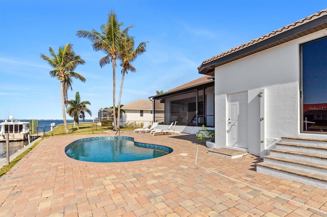 view of pool featuring a water view, a patio area, and a sunroom