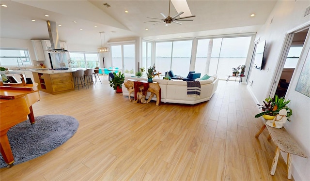 living room with ceiling fan, vaulted ceiling, a wall of windows, and light wood-type flooring