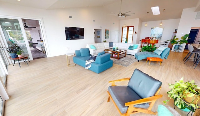 living room with ceiling fan, light wood-type flooring, and vaulted ceiling with skylight