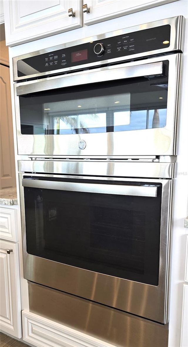 room details with white cabinetry, light stone counters, and stainless steel double oven