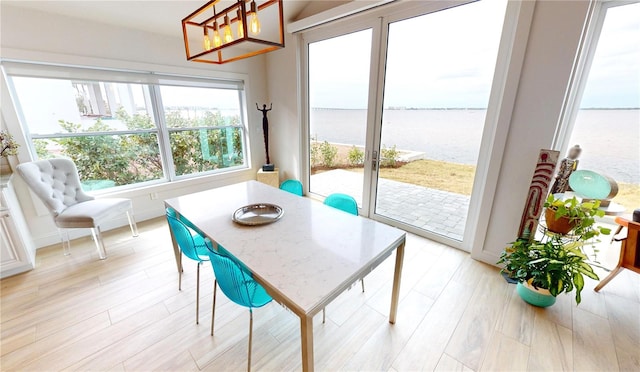 dining room featuring light wood-type flooring, a water view, and a notable chandelier