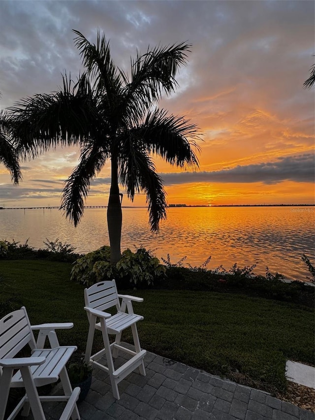 patio terrace at dusk featuring a water view and a yard