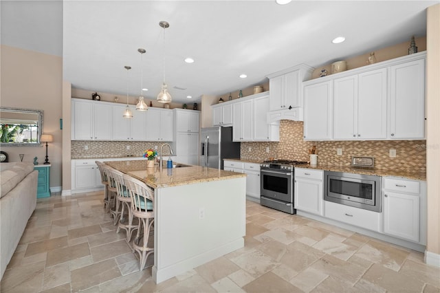 kitchen with white cabinets, pendant lighting, a breakfast bar area, a kitchen island with sink, and appliances with stainless steel finishes