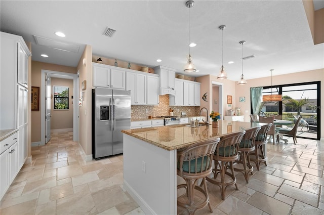 kitchen with hanging light fixtures, a kitchen island with sink, white cabinets, appliances with stainless steel finishes, and sink