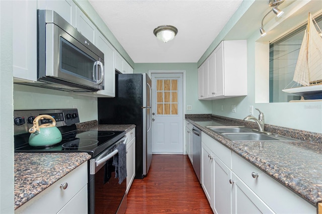 kitchen featuring appliances with stainless steel finishes, white cabinetry, sink, dark hardwood / wood-style flooring, and dark stone counters