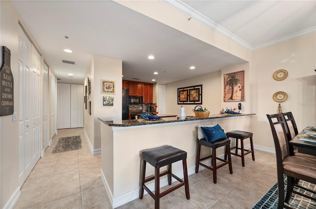 kitchen featuring light tile patterned floors, visible vents, dark stone countertops, a peninsula, and a kitchen breakfast bar