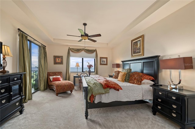 bedroom with access to exterior, a tray ceiling, light carpet, and ceiling fan