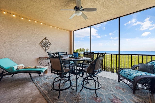 sunroom / solarium with a ceiling fan and a water view