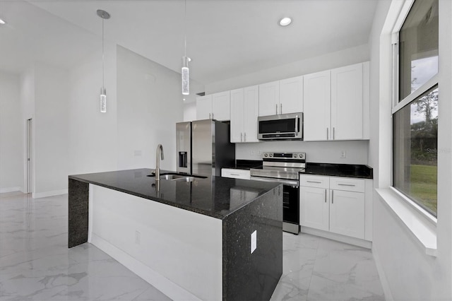 kitchen with pendant lighting, sink, appliances with stainless steel finishes, an island with sink, and dark stone counters