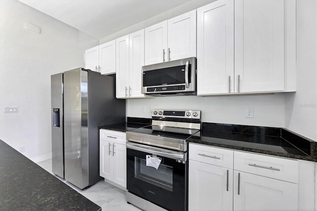 kitchen with stainless steel appliances, dark stone counters, and white cabinets