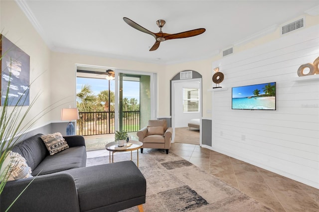 living room with wooden walls, ceiling fan, light tile patterned floors, and crown molding