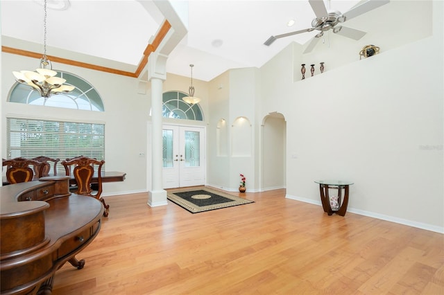 foyer entrance with high vaulted ceiling, ceiling fan with notable chandelier, light hardwood / wood-style floors, and french doors