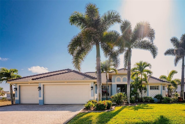 mediterranean / spanish-style house featuring a garage, stucco siding, a tile roof, decorative driveway, and a front yard