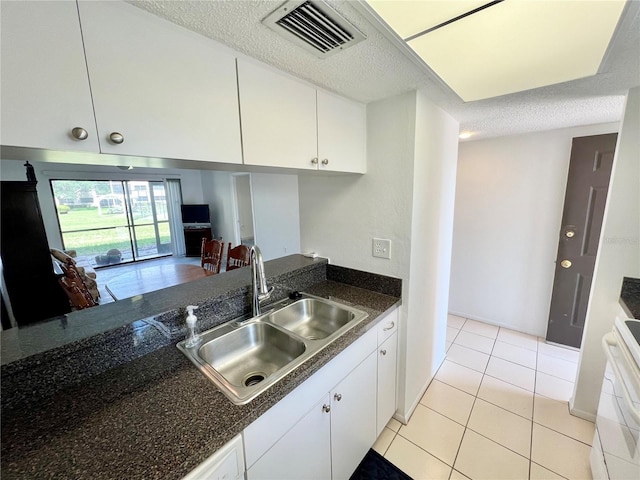 kitchen with a textured ceiling, range, light tile patterned floors, white cabinetry, and sink