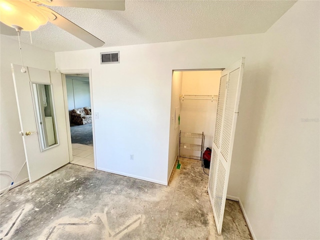 unfurnished bedroom featuring a walk in closet, a closet, ceiling fan, and a textured ceiling