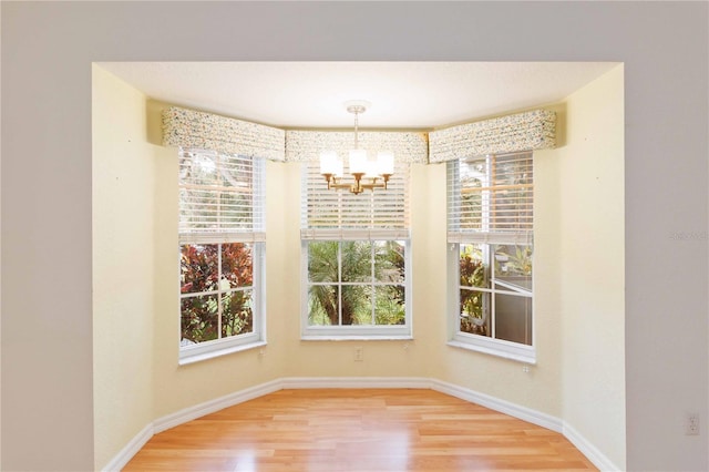 unfurnished dining area featuring plenty of natural light, wood-type flooring, and a notable chandelier