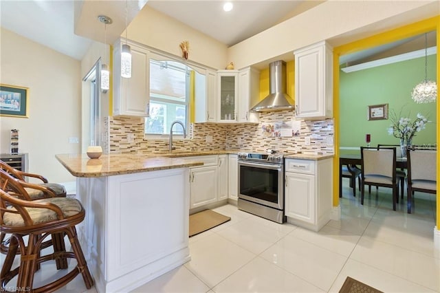 kitchen with kitchen peninsula, electric stove, pendant lighting, wall chimney range hood, and white cabinets