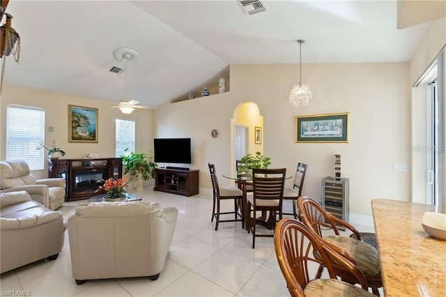 tiled living room with a fireplace, lofted ceiling, ceiling fan with notable chandelier, and wine cooler