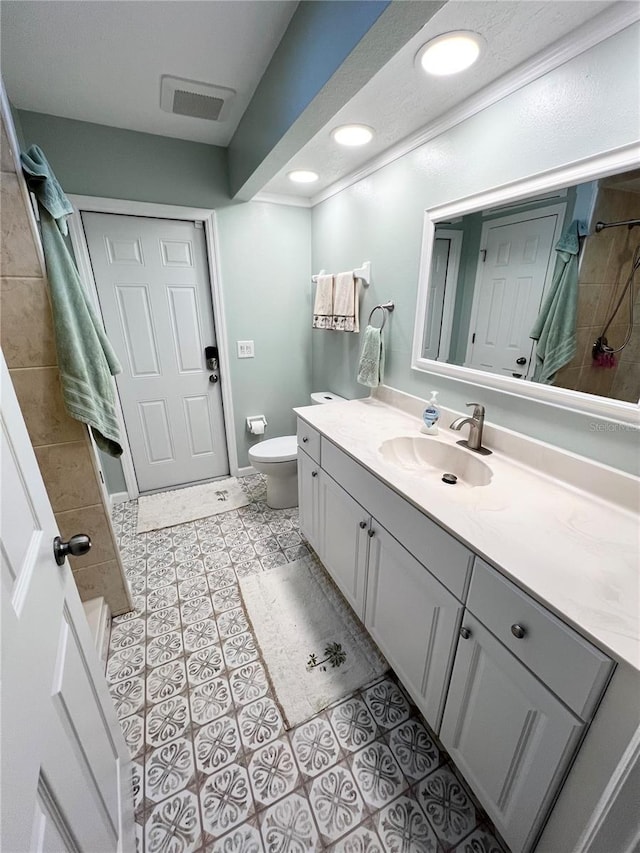 bathroom featuring vanity, a tile shower, tile patterned floors, and toilet