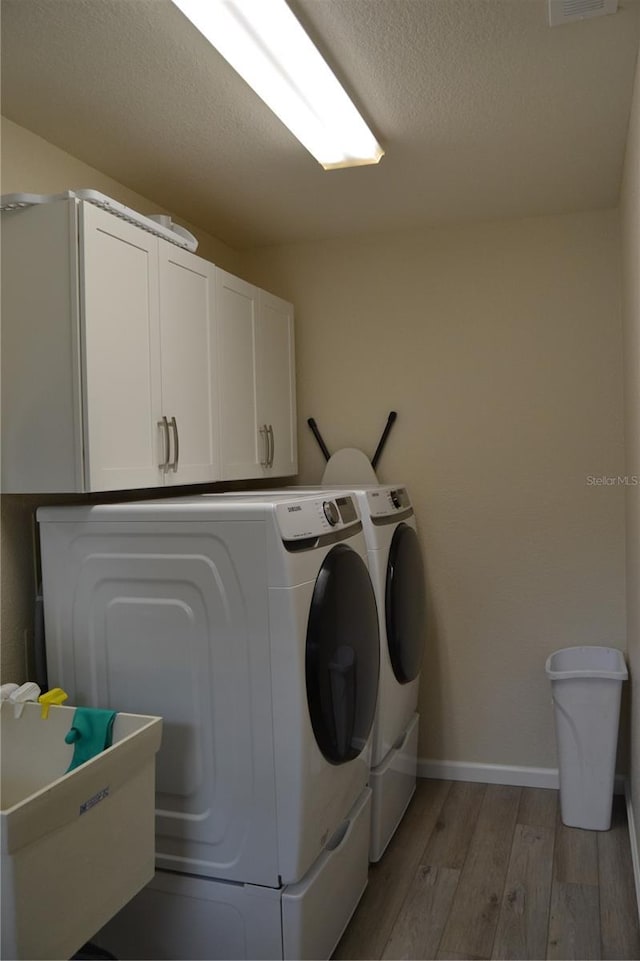 washroom with sink, cabinets, light hardwood / wood-style flooring, a textured ceiling, and washer and clothes dryer