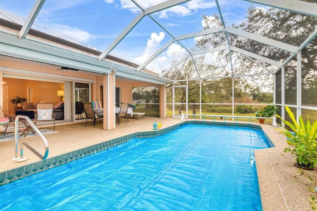 view of swimming pool with ceiling fan, glass enclosure, and a patio area