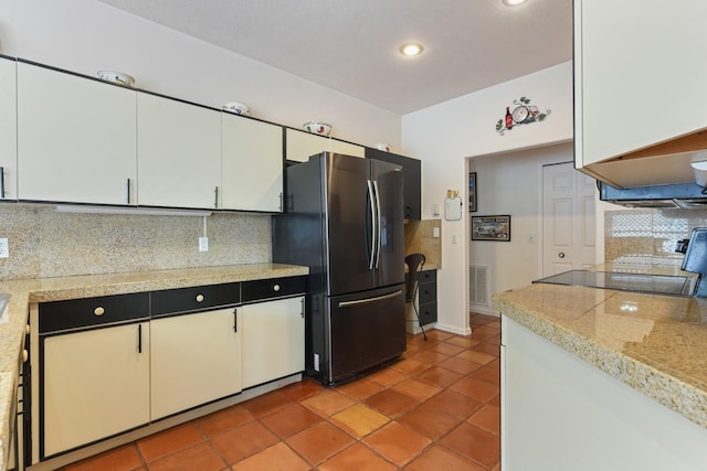 kitchen featuring backsplash, white cabinetry, black fridge, and tile patterned flooring