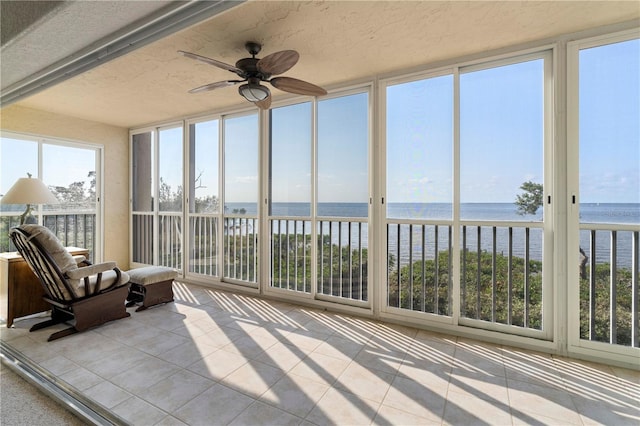 sunroom with ceiling fan and a water view