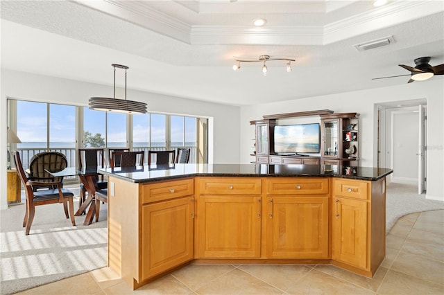 kitchen with dark stone counters, a kitchen island, a tray ceiling, and hanging light fixtures