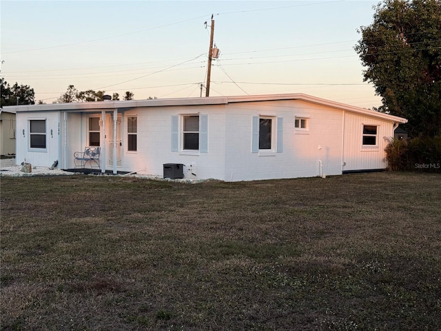 back house at dusk with a porch, central air condition unit, and a lawn