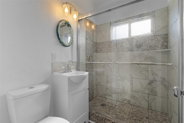 full bathroom featuring toilet, a textured wall, a shower stall, and vanity