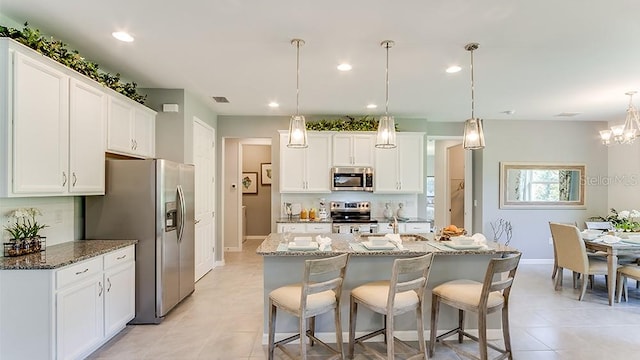 kitchen with stainless steel appliances, dark stone countertops, white cabinets, and hanging light fixtures