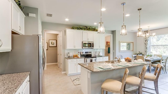 kitchen featuring light stone countertops, pendant lighting, stainless steel appliances, an island with sink, and white cabinets