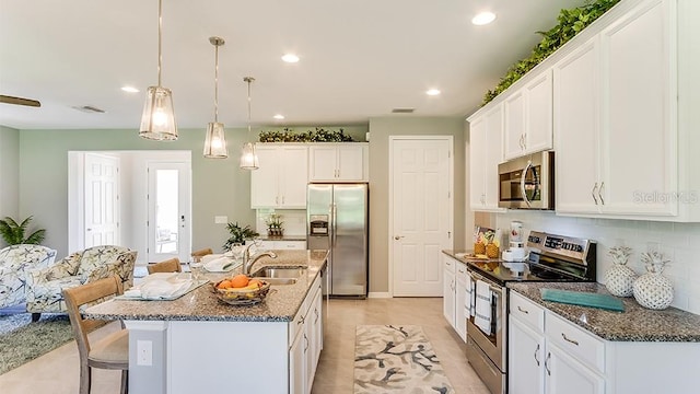 kitchen with appliances with stainless steel finishes, an island with sink, decorative backsplash, white cabinets, and sink