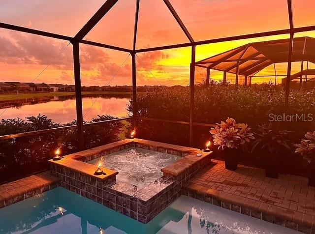 exterior space with glass enclosure, a pool with hot tub, and a water view