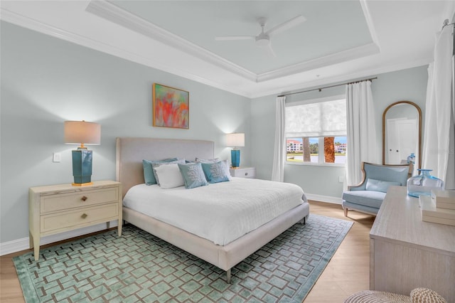 bedroom featuring a raised ceiling, ornamental molding, ceiling fan, and light wood-type flooring