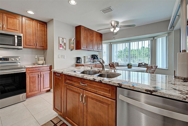 kitchen with sink, light tile patterned floors, ceiling fan, appliances with stainless steel finishes, and light stone countertops