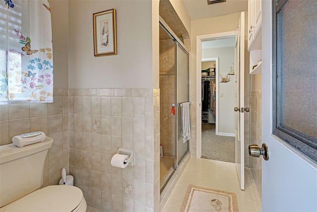 bathroom with toilet, tile patterned flooring, a shower with door, and tile walls