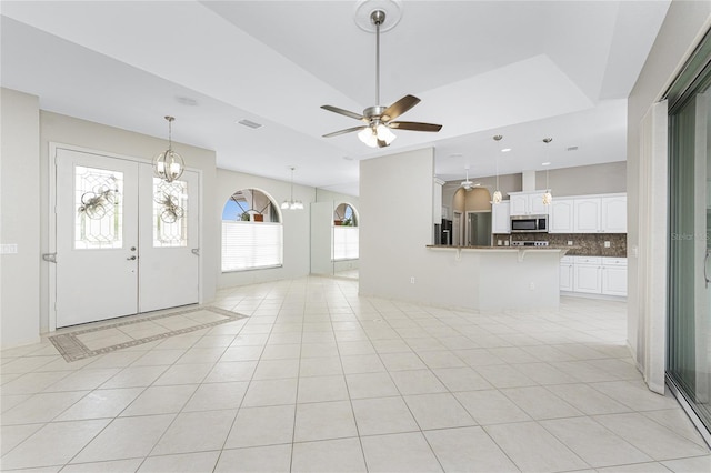 unfurnished living room featuring light tile patterned flooring, ceiling fan with notable chandelier, and french doors