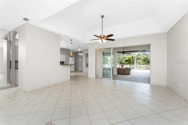 empty room with ceiling fan, light tile patterned floors, and a tray ceiling