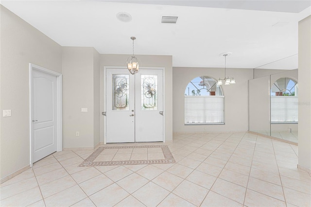 foyer with light tile patterned floors, a notable chandelier, and french doors