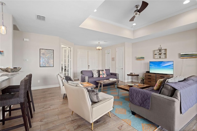 living room with ornamental molding, a tray ceiling, ceiling fan with notable chandelier, and light wood-type flooring